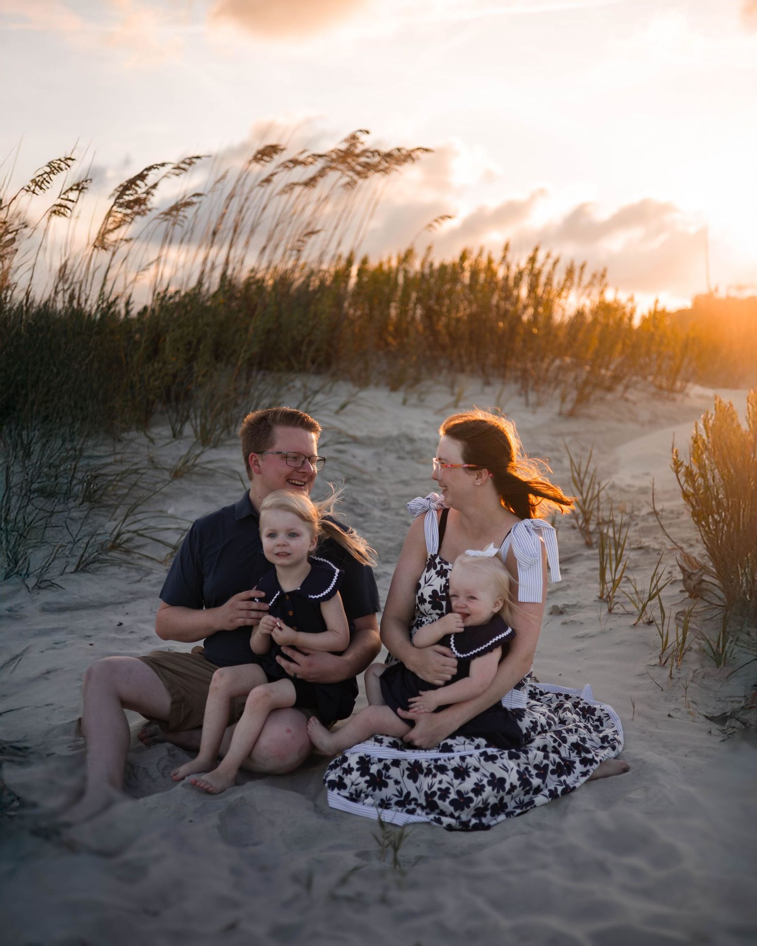 Family shares intimate moment while sitting together on beach sand at sunset.