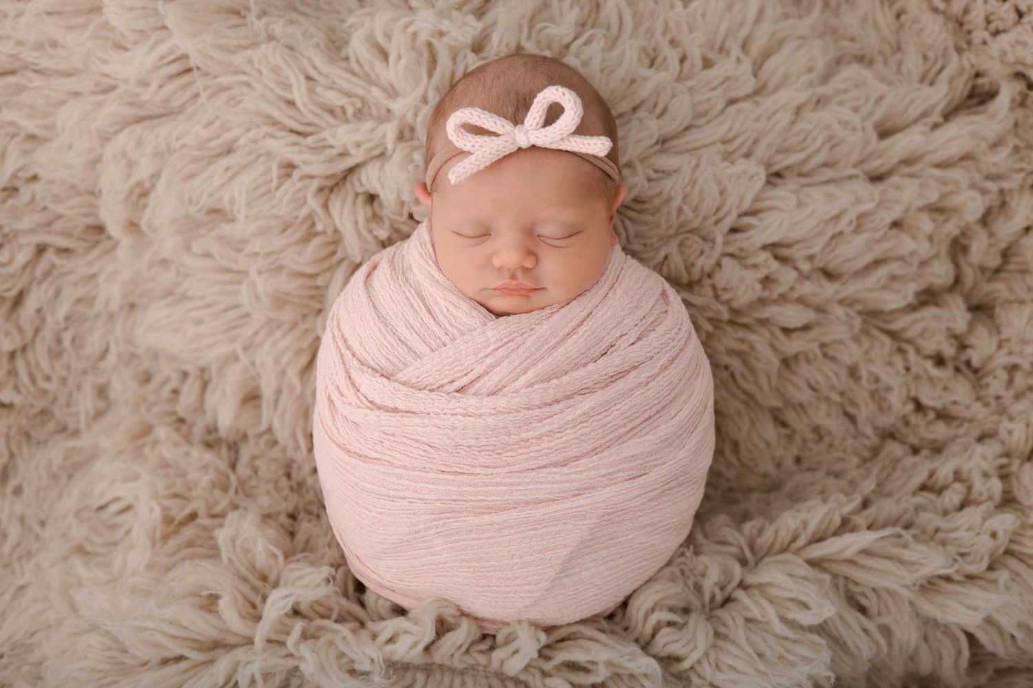 A series of newborn photography portraits showing a baby wrapped in soft pink fabric on cream textured blankets.
