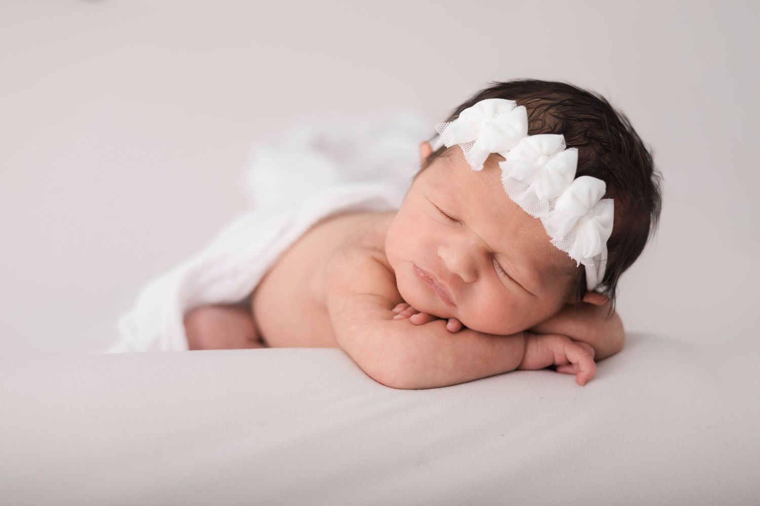 A series of minimalist newborn baby photos showing gentle poses on soft white fabric in natural lighting.
