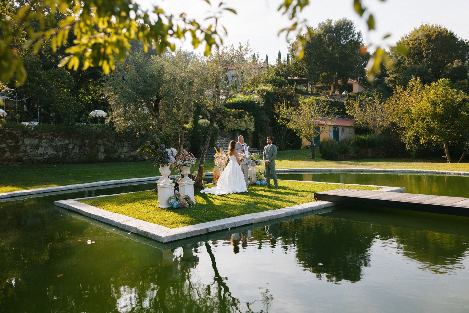 Bride and wedding party gathered on a scenic grass island platform surrounded by a tranquil garden pond.