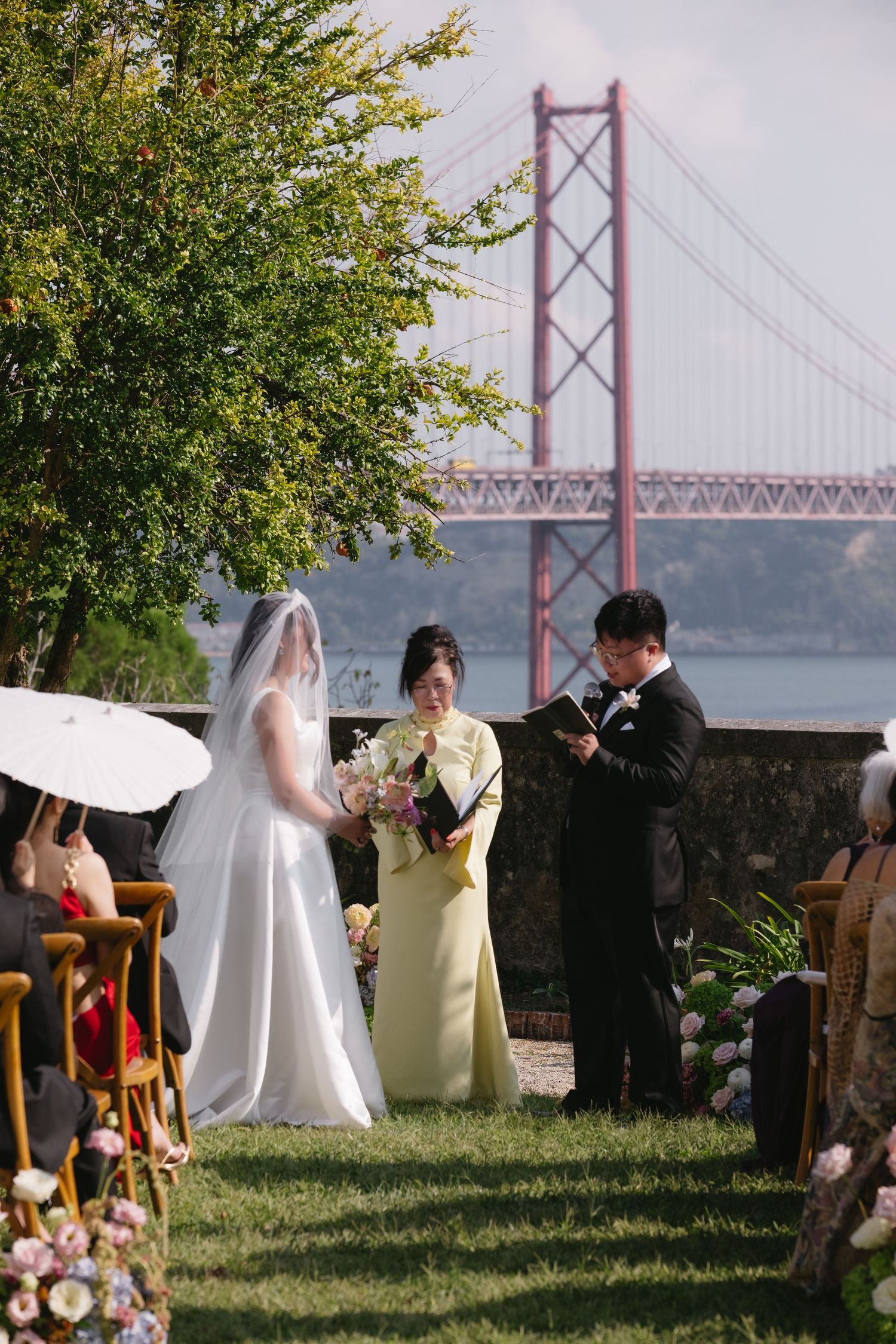 Outdoor wedding ceremony with bride and groom exchanging vows near the 25 de Abril Bridge in Lisbon, Portugal.