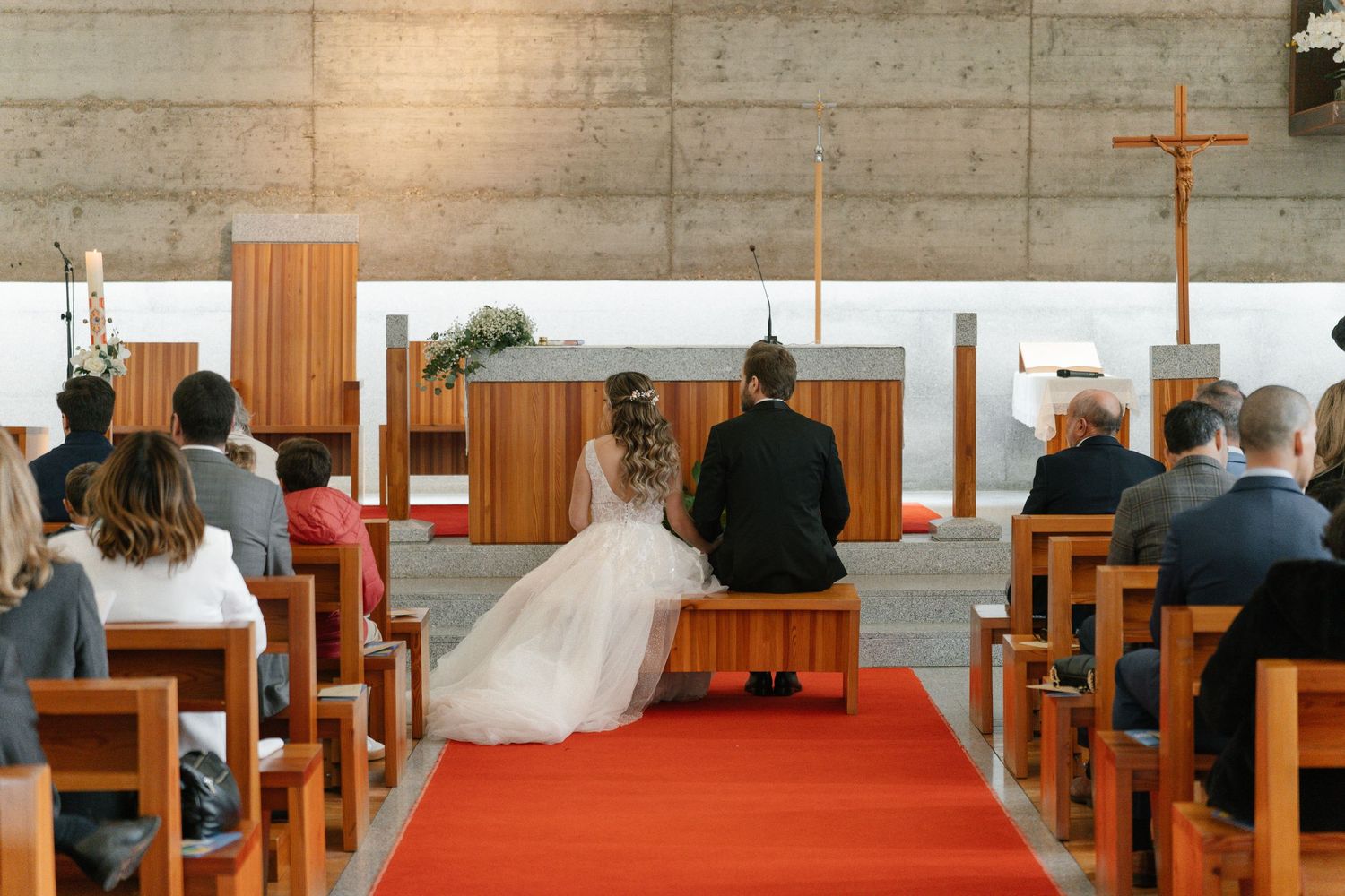 Bride and groom kneel at altar during church wedding ceremony with guests seated.