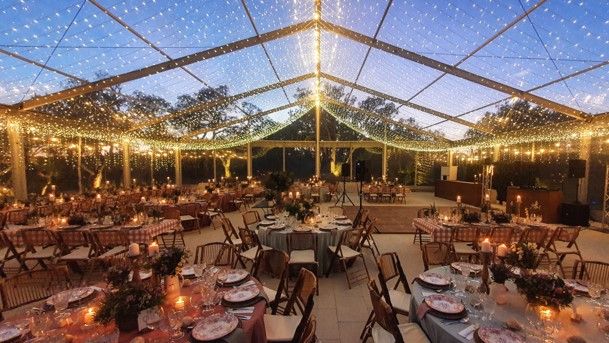 Magical transparent wedding tent adorned with fairy lights and elegant table settings glowing at dusk.