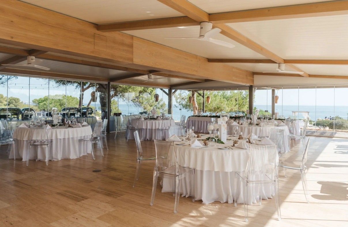 Elegant open-air wedding reception hall with round tables, white linens, and ocean views.