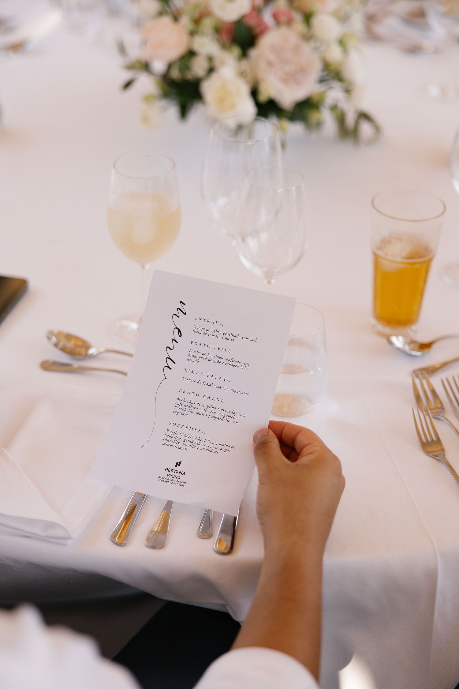 Guest reads elegant wedding reception menu card at beautifully set table with floral centerpiece and champagne glasses.