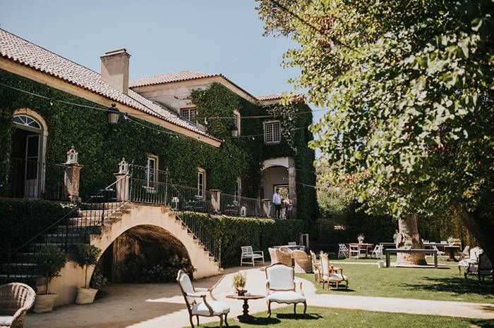 Ivy-covered wedding venue with arched colonnade, manicured gardens, and elegant vintage outdoor furniture.