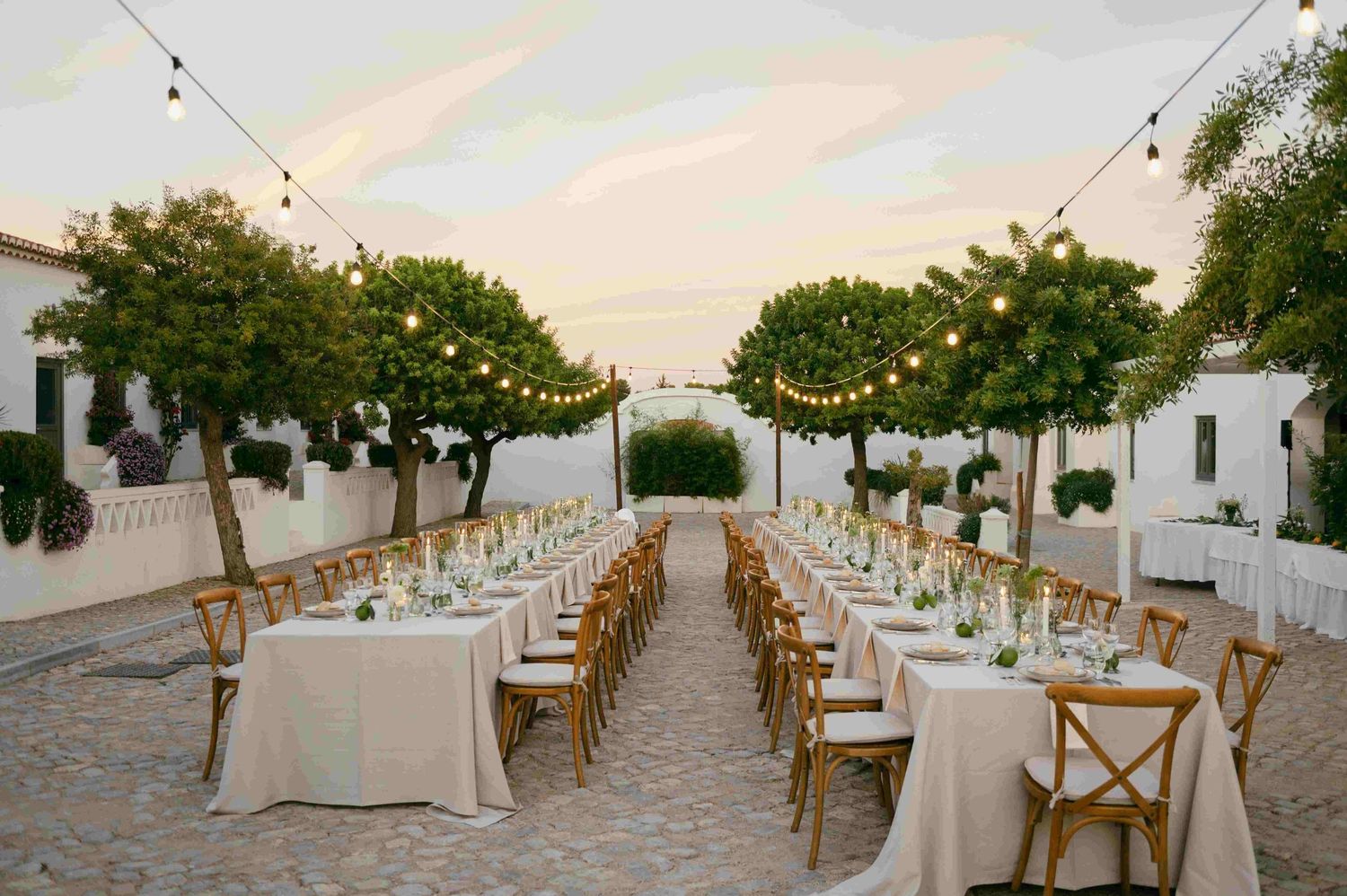 Elegant outdoor wedding reception with long tables and string lights at dusk.