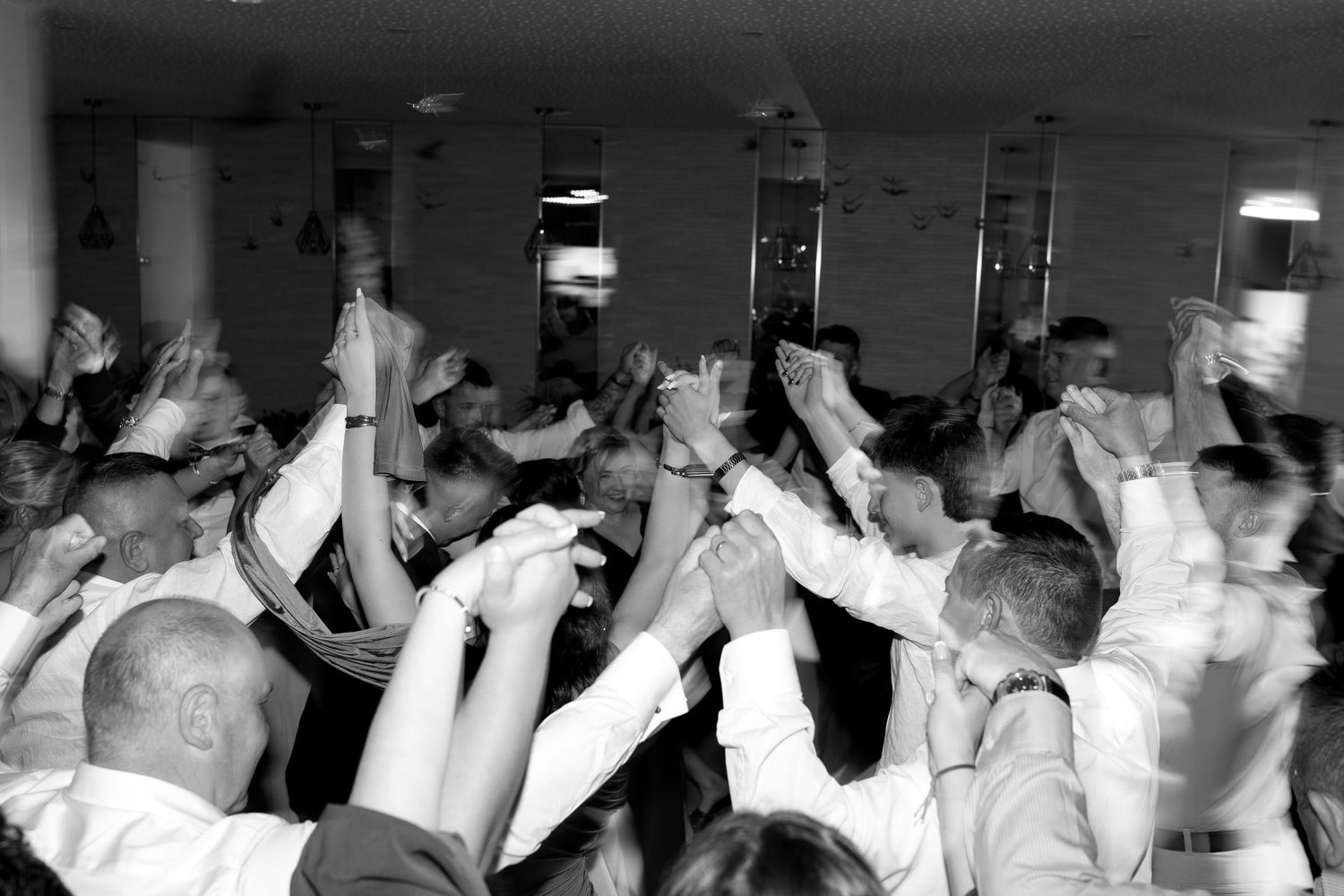 Black and white photo of wedding guests dancing and raising hands at a lively reception party.