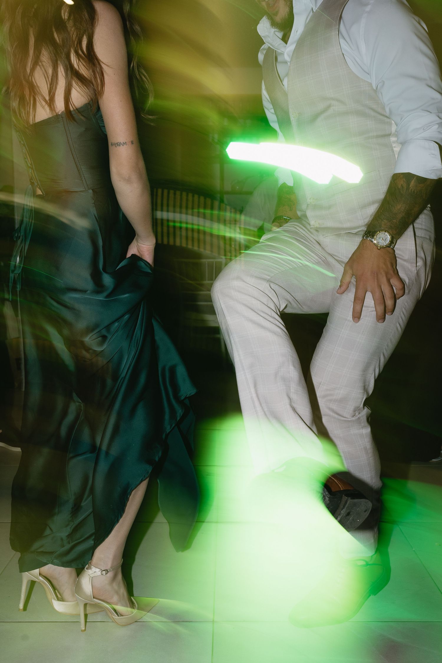 Couple dancing under green neon lights, woman in emerald gown and man in white shirt and pants.