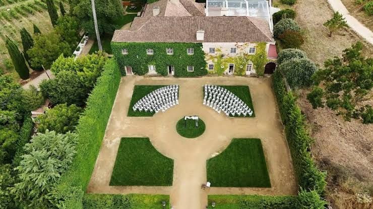Aerial view of ivy-covered estate with formal geometric gardens and white chairs arranged for an outdoor ceremony.