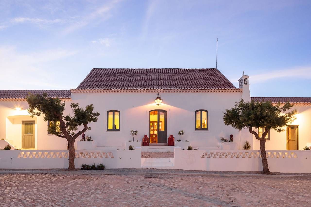 Charming white Portuguese farmhouse exterior illuminated at twilight with cobblestone courtyard.