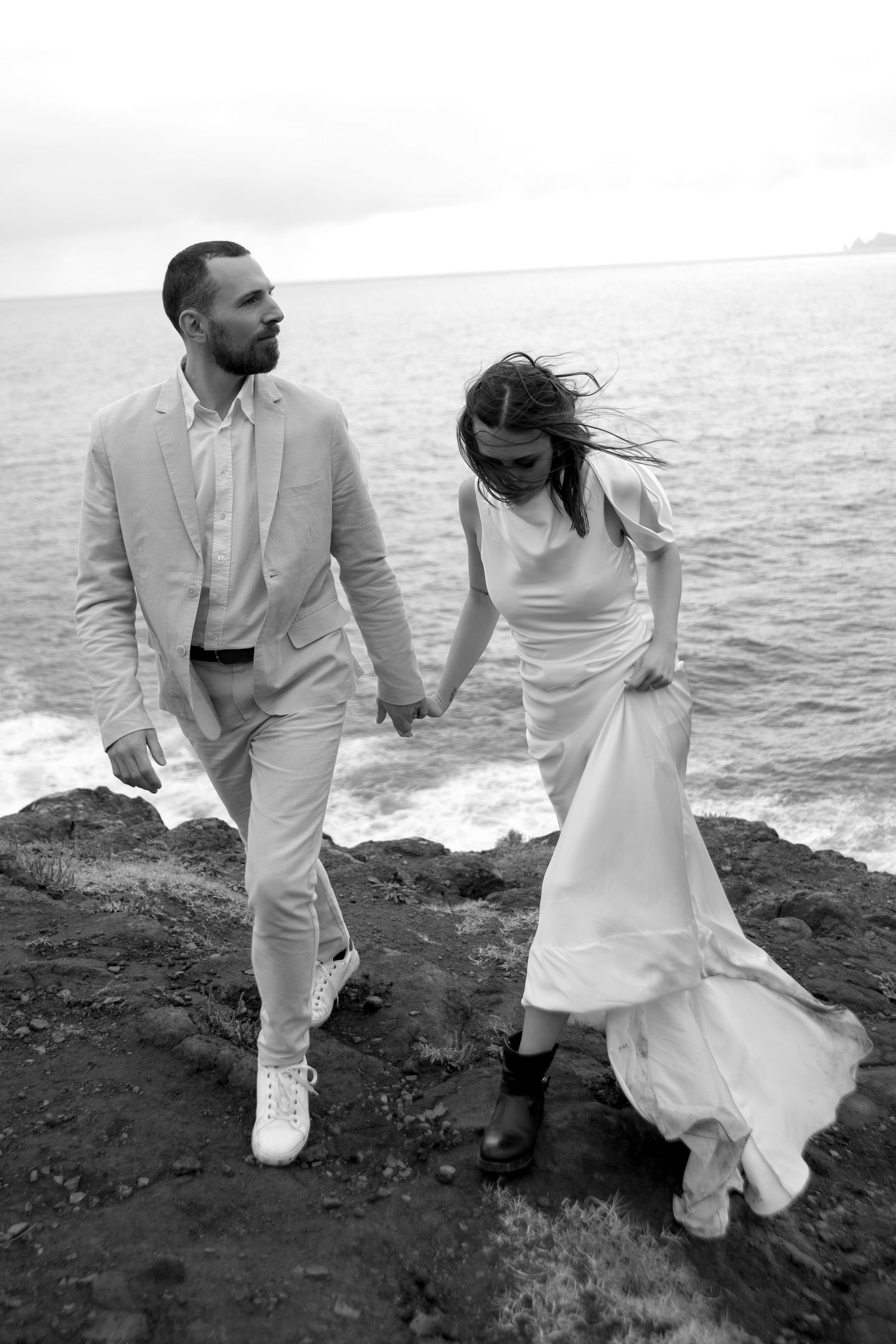 Black and white photo of couple holding hands on rocky ocean cliffs.