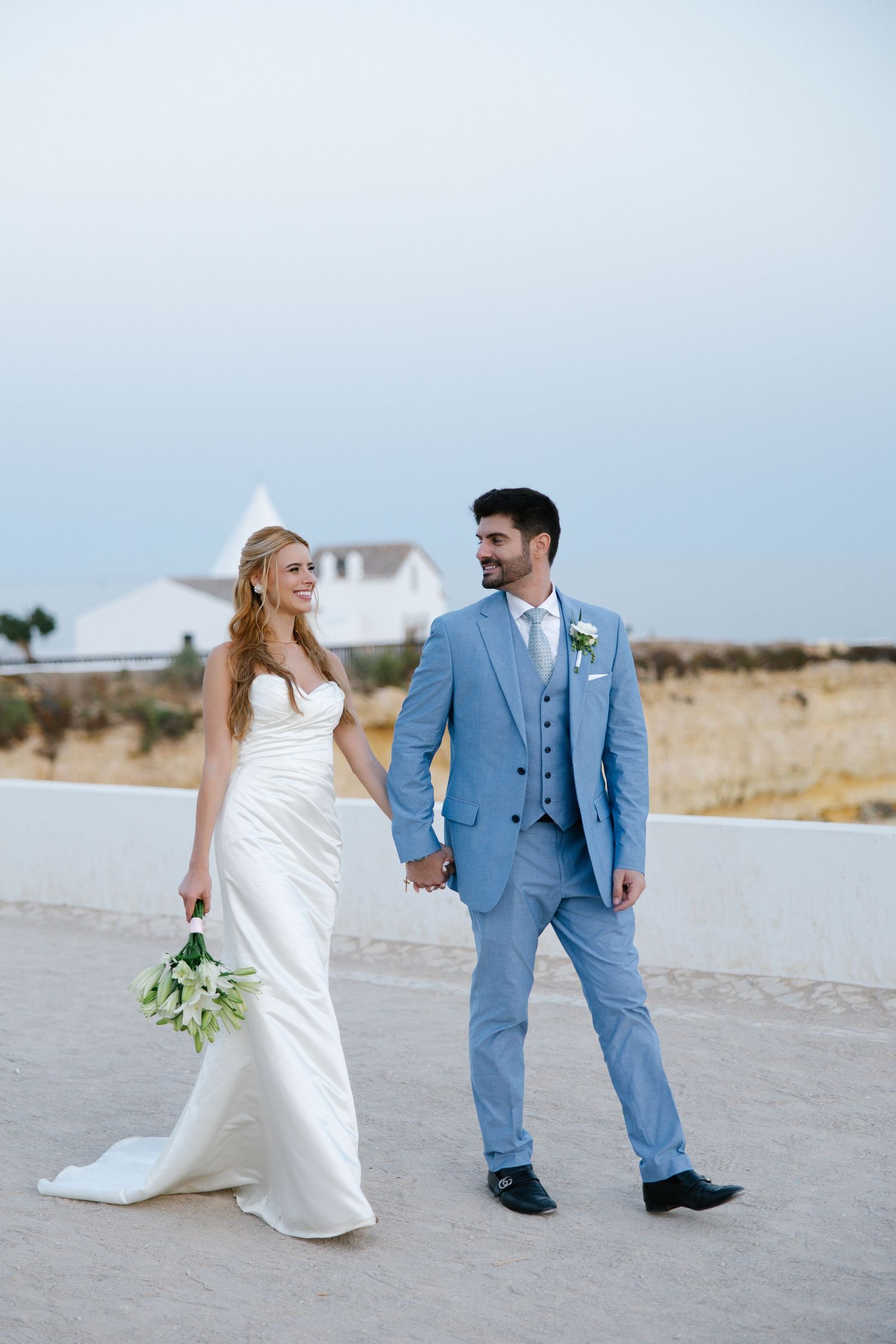Romantic bride and groom walking together on the cliffs of Nossa Senhora on their wedding day taken by Wedding photographer Algarve