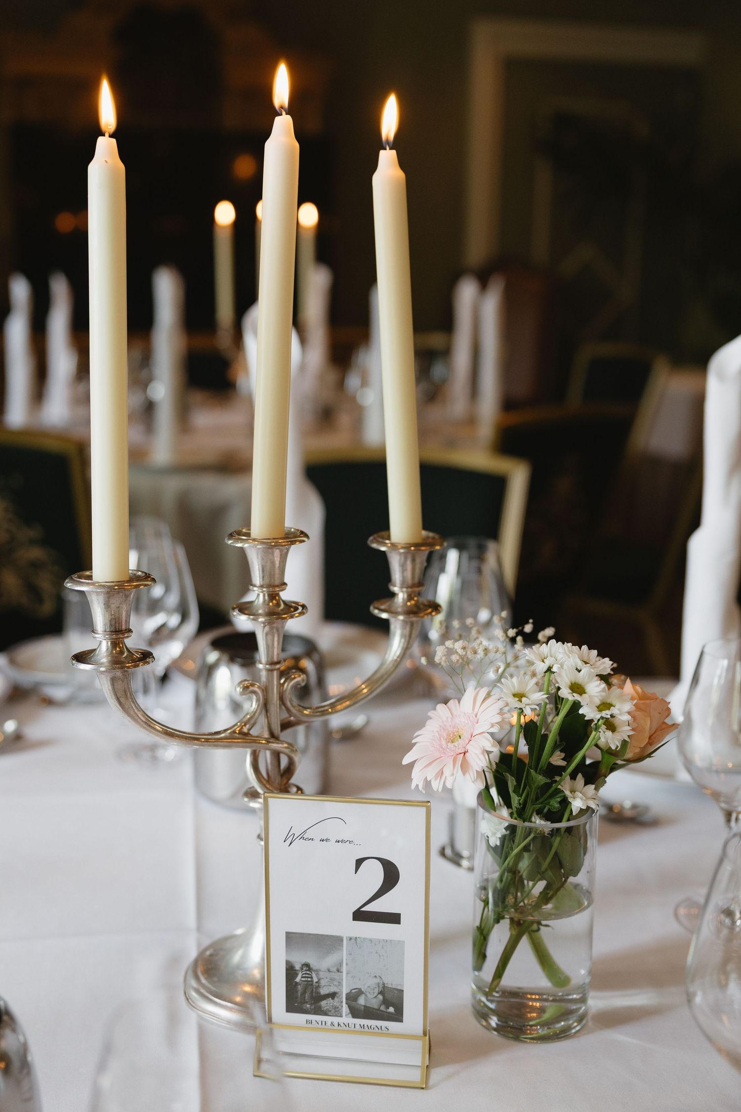 Elegant wedding table setting with silver candelabra, lit taper candles, table number card, and pink floral centerpiece.