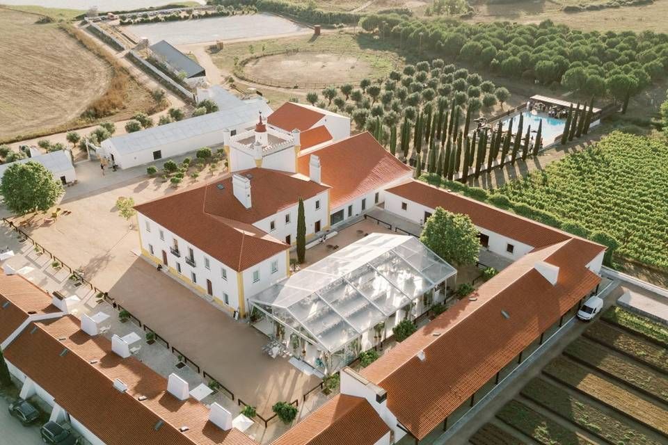 Aerial view of a Portuguese wine estate with red-tiled roofs, vineyards, and a glass event pavilion.