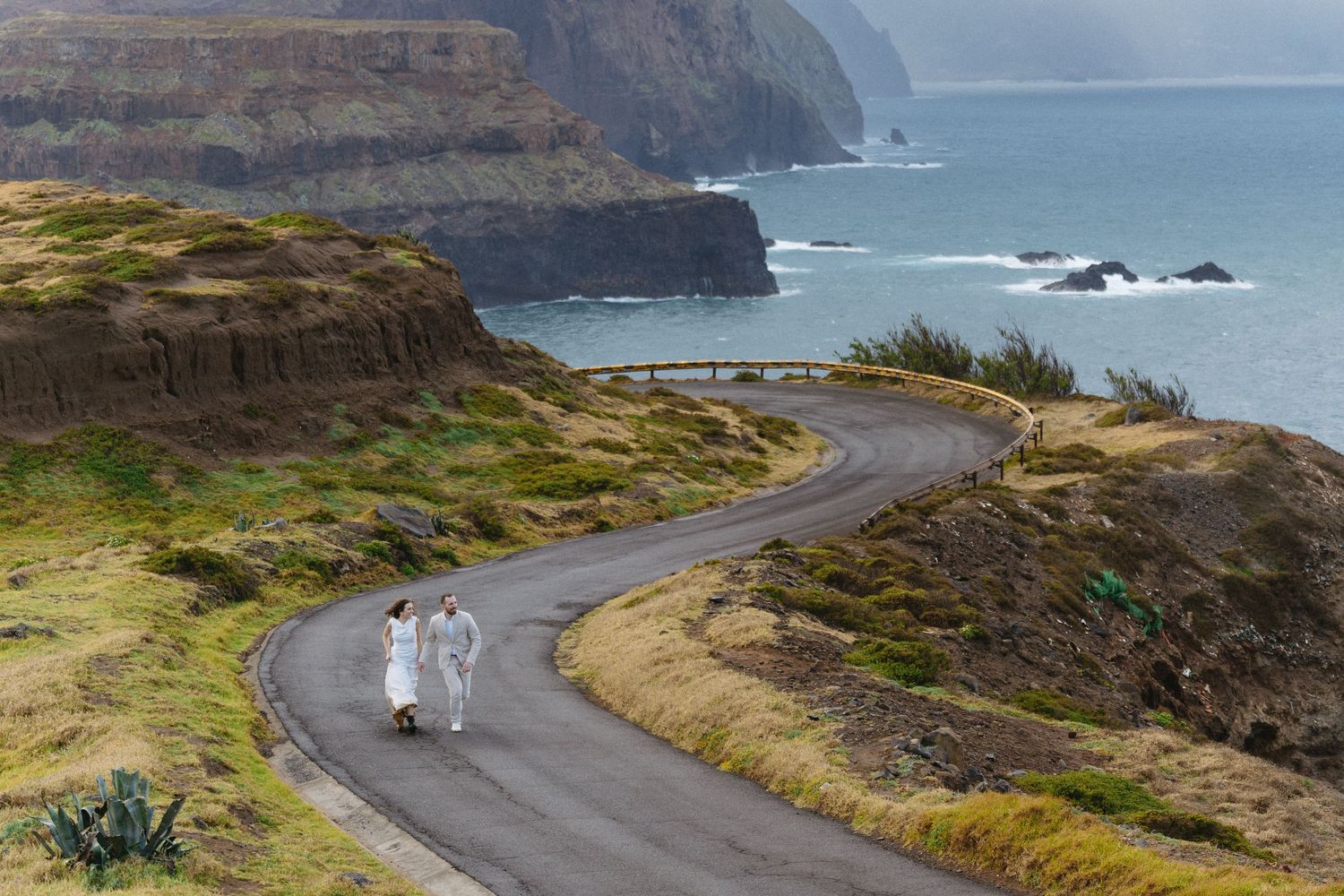 Wedding couple strolling along winding coastal road with stunning ocean cliffs in Madeira.