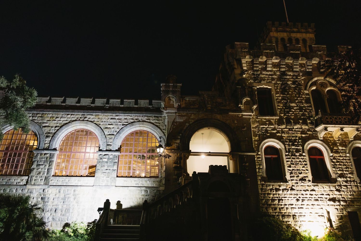 Historic stone castle illuminated at night with arched windows and warm golden lighting against a dark sky.