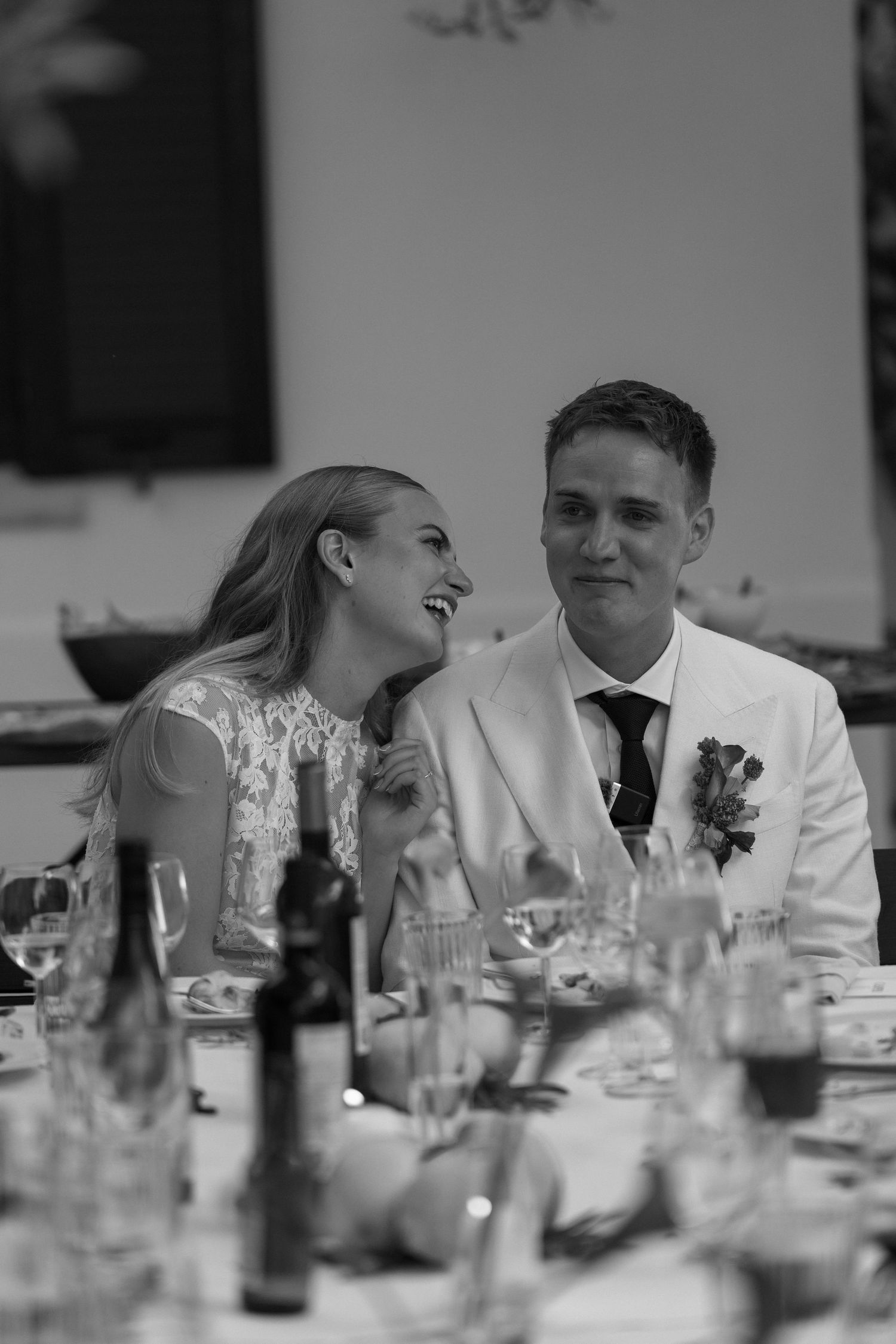 Black and white photo of a bride and groom laughing together at their wedding reception dinner.