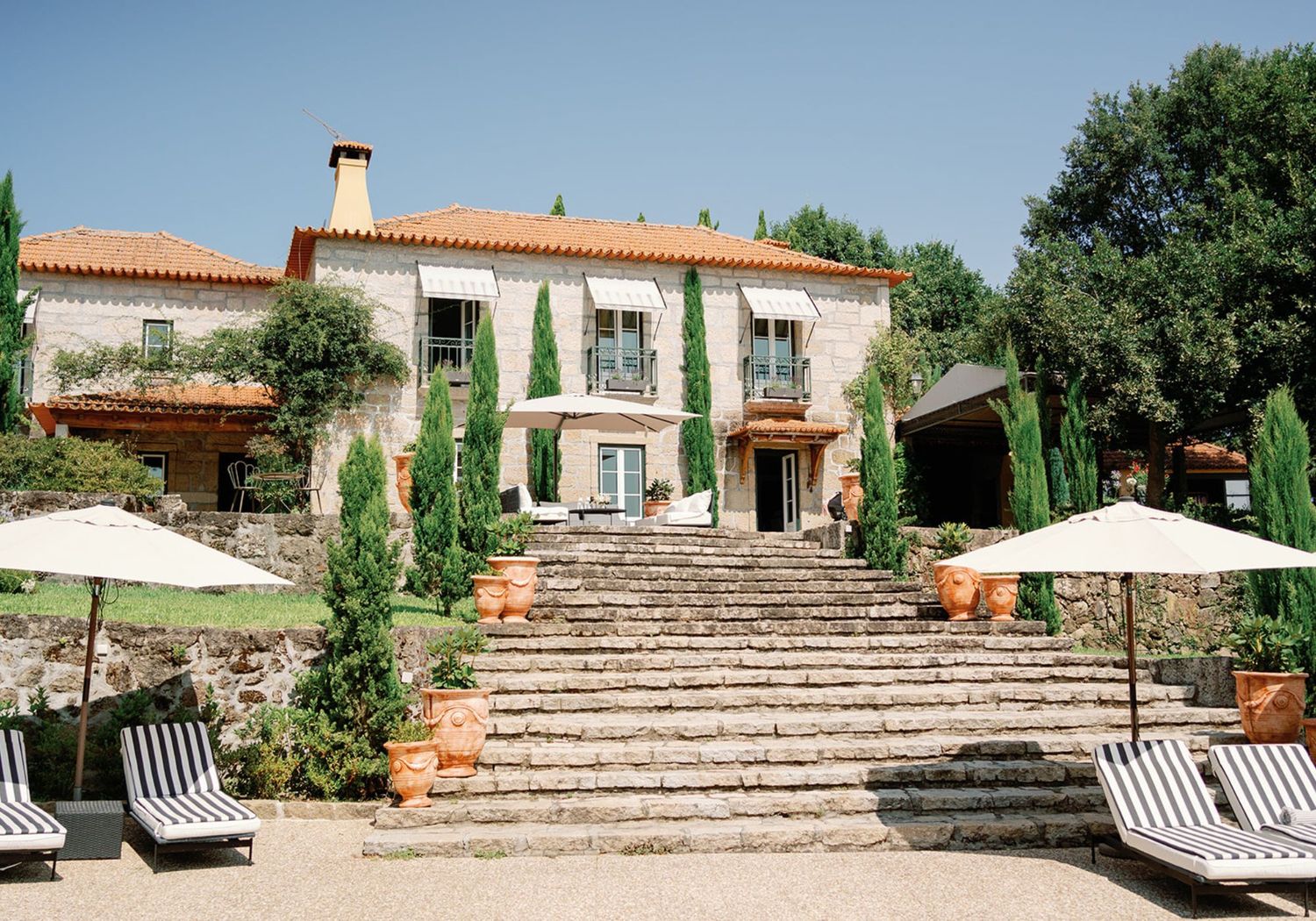 Elegant Mediterranean wedding estate featuring grand stone staircase, cypress trees, and sun-drenched terrace with umbrellas.