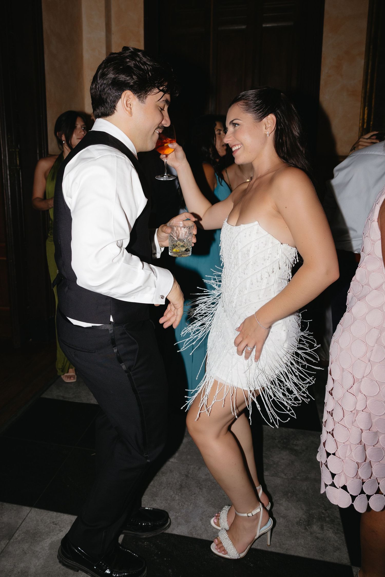 Couple dancing at formal event, woman in white feathered mini dress, man in black vest and white shirt.
