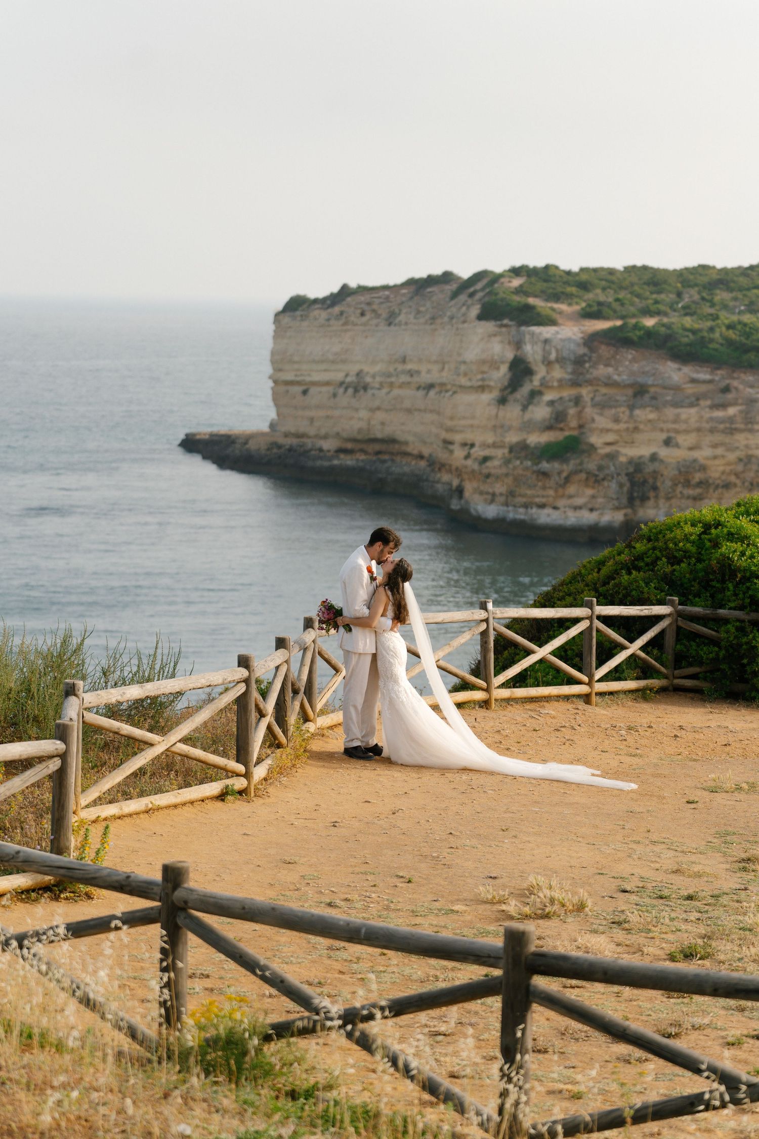 Kiss of bride and groom on the cliffs of Nossa Senhora beach in the Algarve