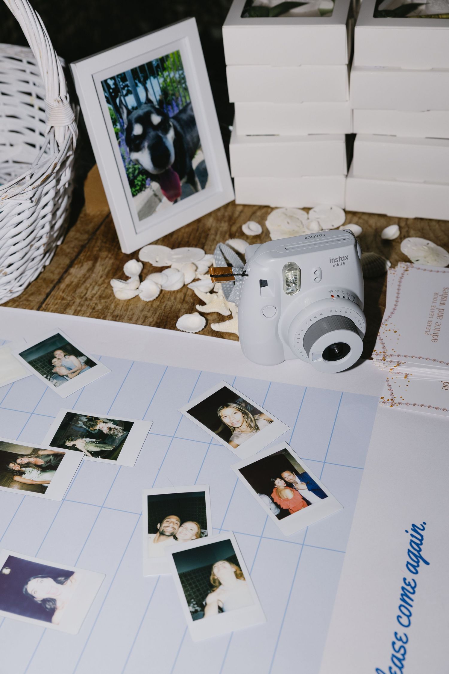 Fujifilm Instax mini camera surrounded by polaroid photos on a lined guestbook at a wedding reception table.
