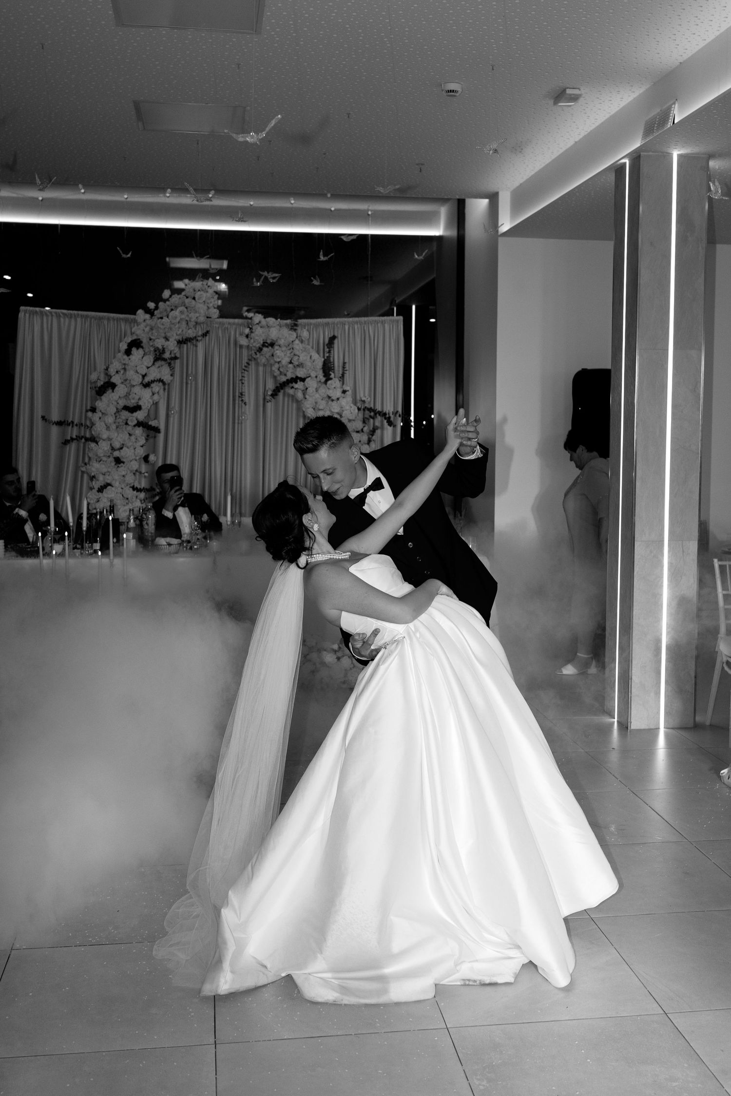 Black and white photo of bride and groom sharing romantic first dance surrounded by dry ice fog.