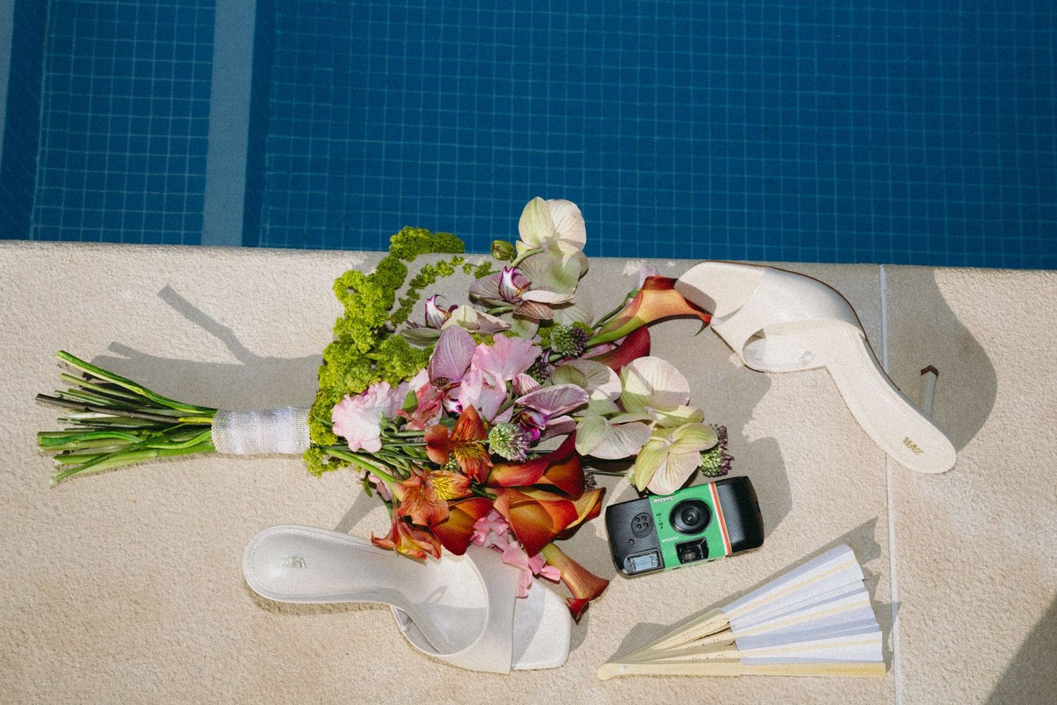Overhead view of colorful bridal bouquet with flowers, ribbons, and disposable camera on poolside.