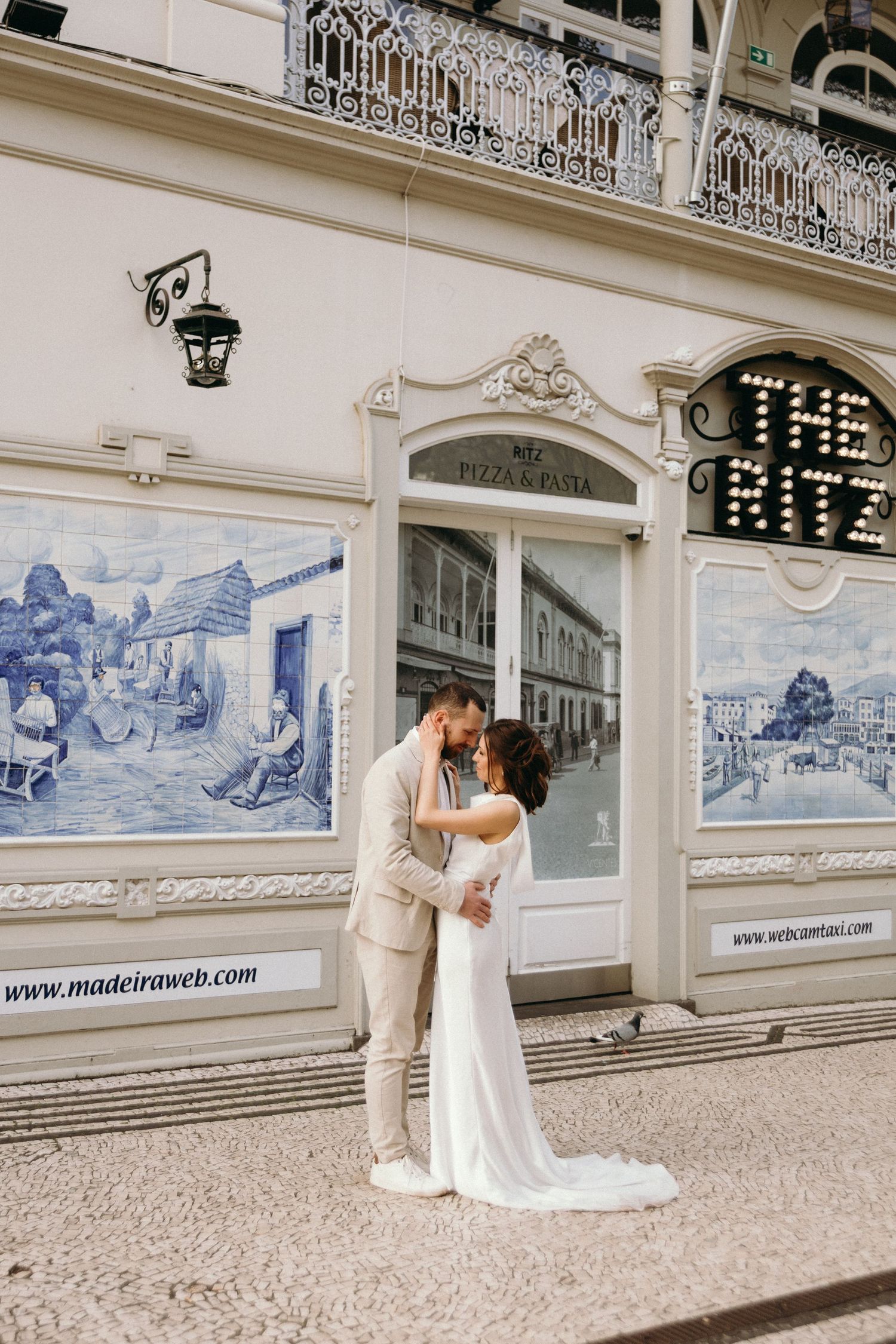 Couple sharing a romantic kiss in wedding attire outside The Ritz in Madeira, Portugal, with traditional azulejo tile murals.