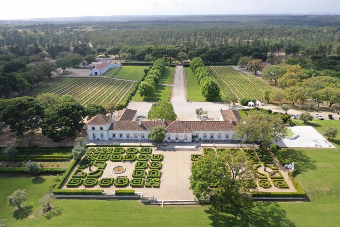 Aerial view of a grand Portuguese estate with formal geometric gardens, long tree-lined driveway and vineyards.