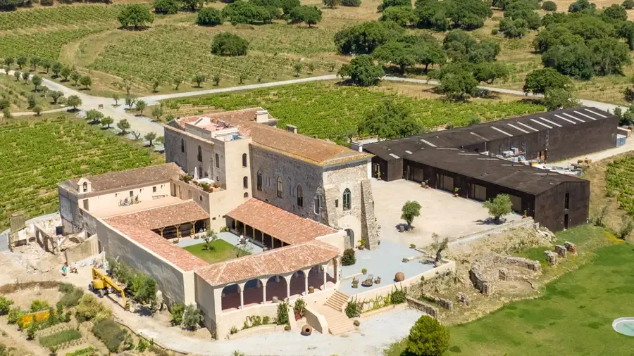 Aerial view of a rustic vineyard wedding venue with stone buildings surrounded by lush vineyards and olive trees.