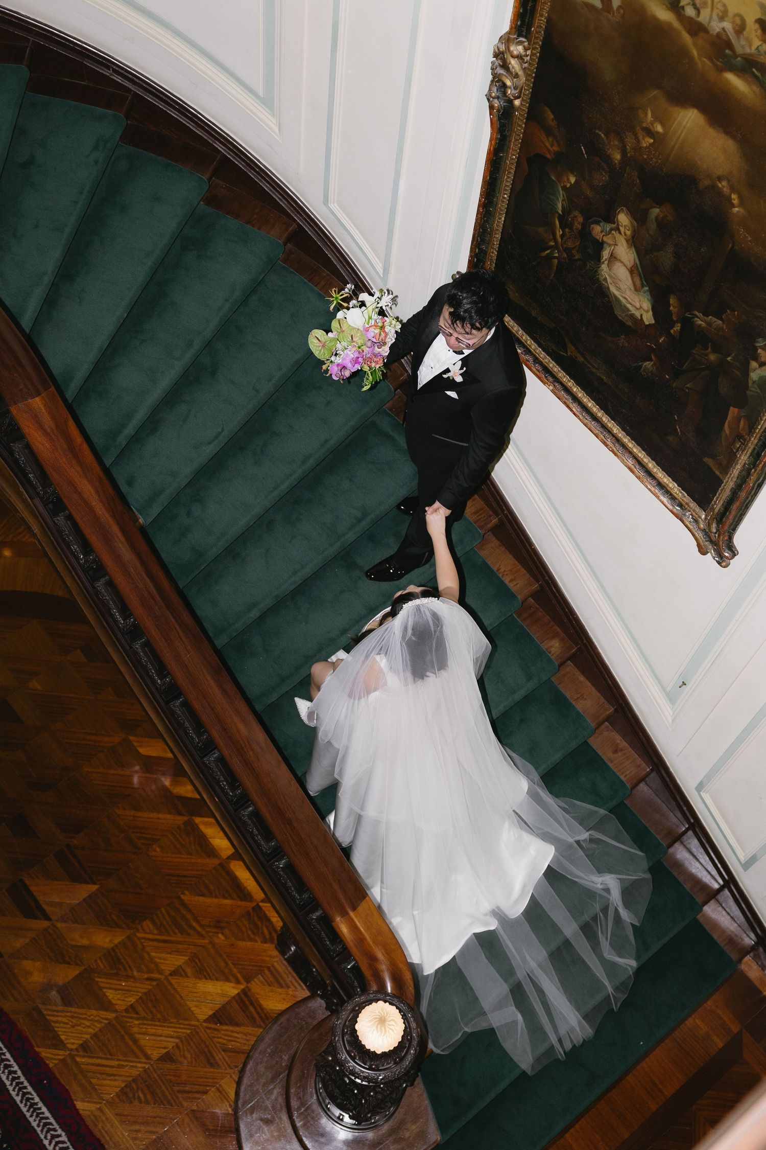 Aerial view of bride and groom descending elegant green carpeted staircase in grand venue on wedding day.