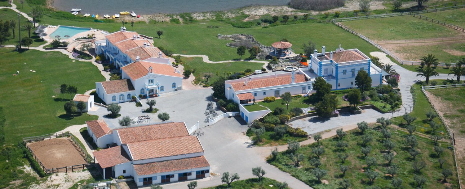 Aerial view of a Portuguese estate with terracotta-roofed buildings, a pool, and lush green surroundings.