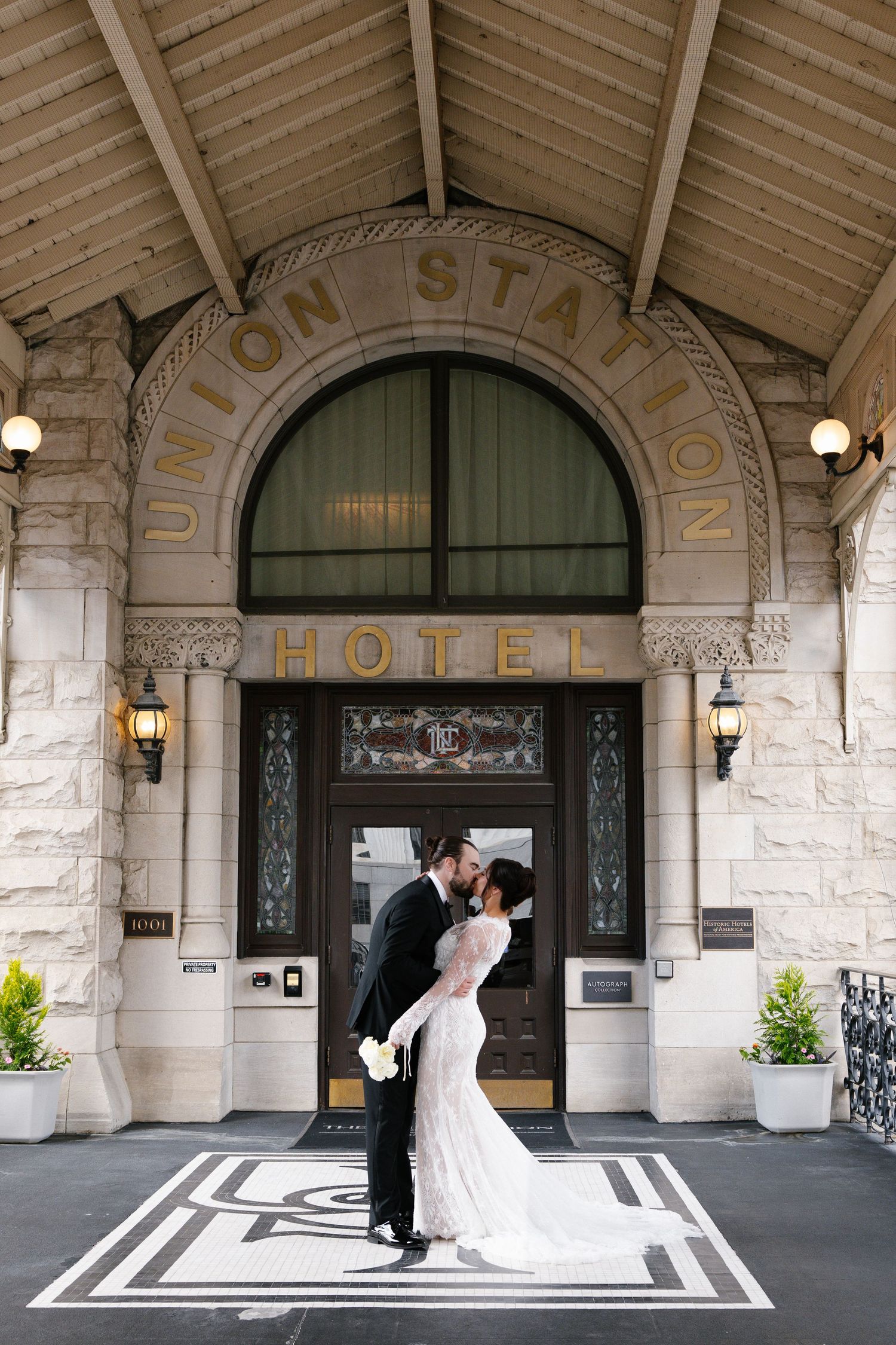 Bride and groom share a romantic kiss at the entrance of Union Station Hotel, a historic stone building with elegant arched doorway.