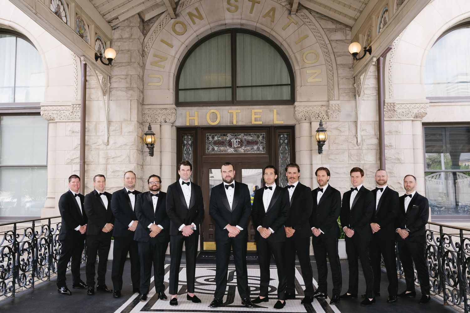 Groom and groomsmen in black tuxedos posing in front of Union Station Hotel entrance.