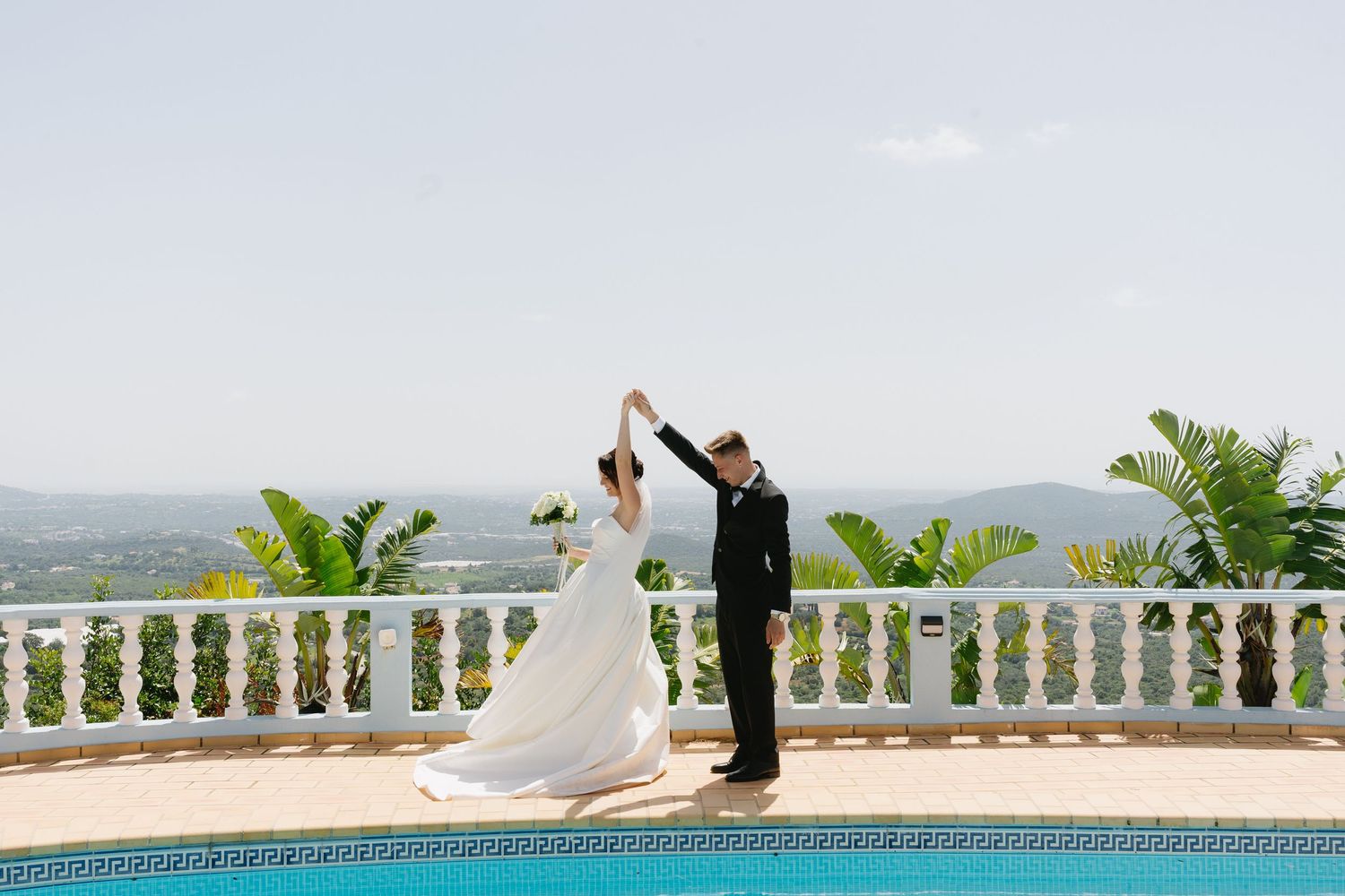 Bride and groom dance elegantly beside a pool with panoramic landscape views on their wedding day.