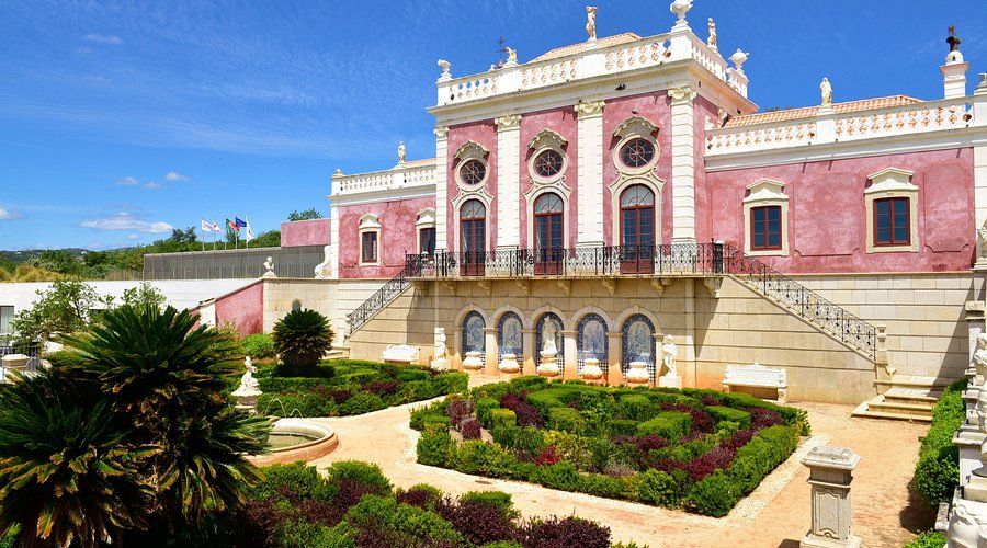 Ornate pink baroque Estoi Palace with formal symmetrical gardens and decorative white stone balustrades.