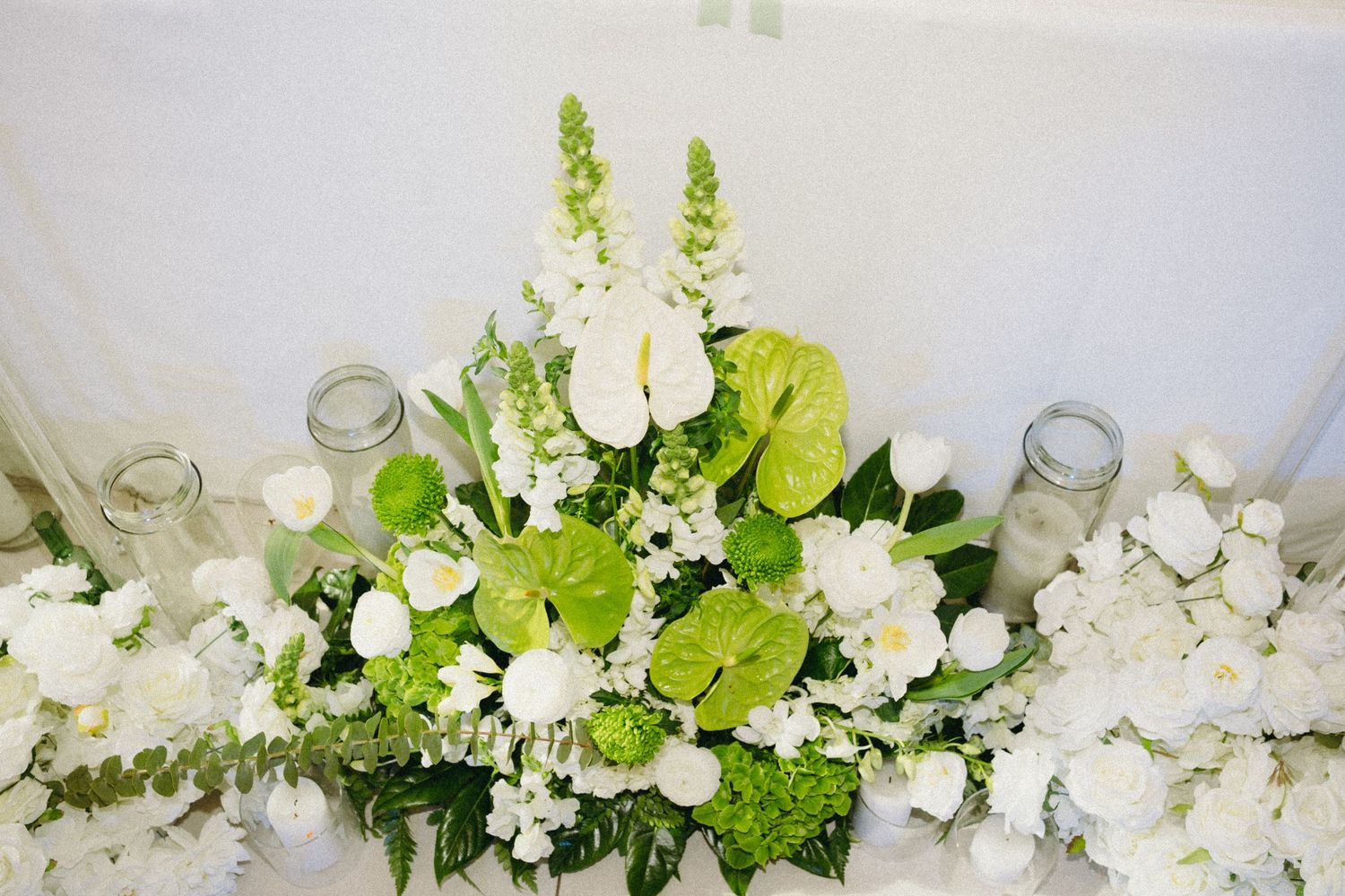 Elegant wedding table centerpiece with white and green flowers including anthuriums and roses.