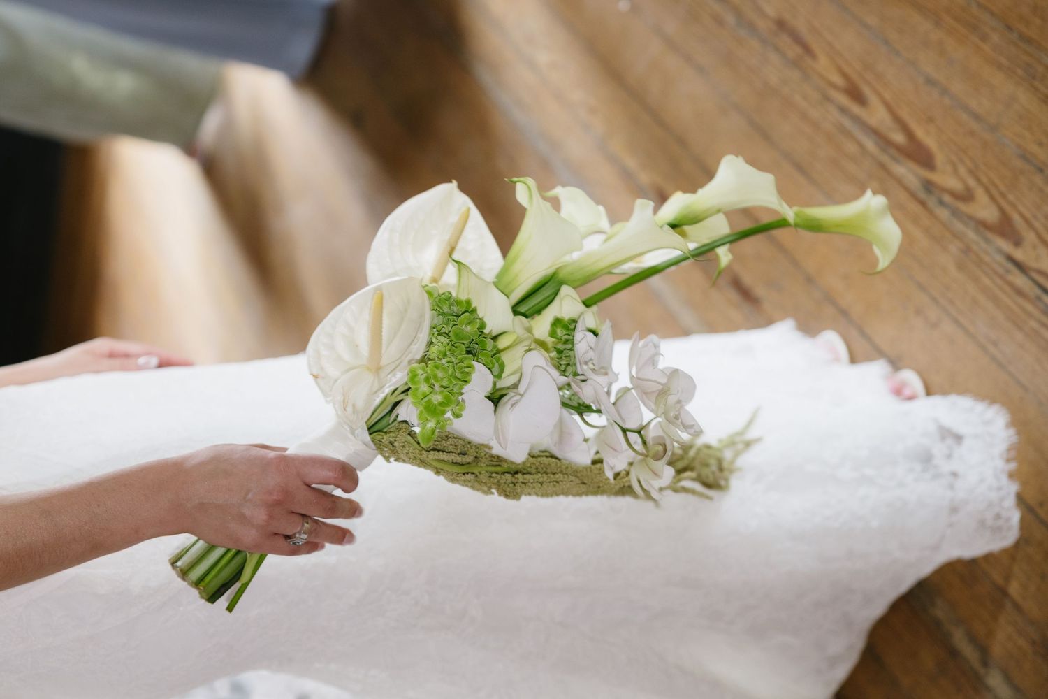 A bride holding a elegant white calla lily and hydrangea wedding bouquet over her lace wedding dress.