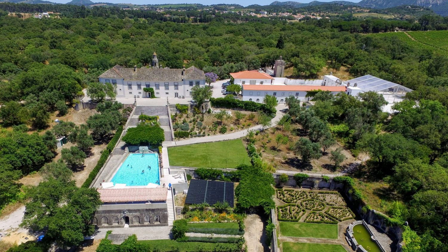 Aerial view of a grand estate with a pool, manicured gardens, and lush green surroundings in a serene countryside setting.