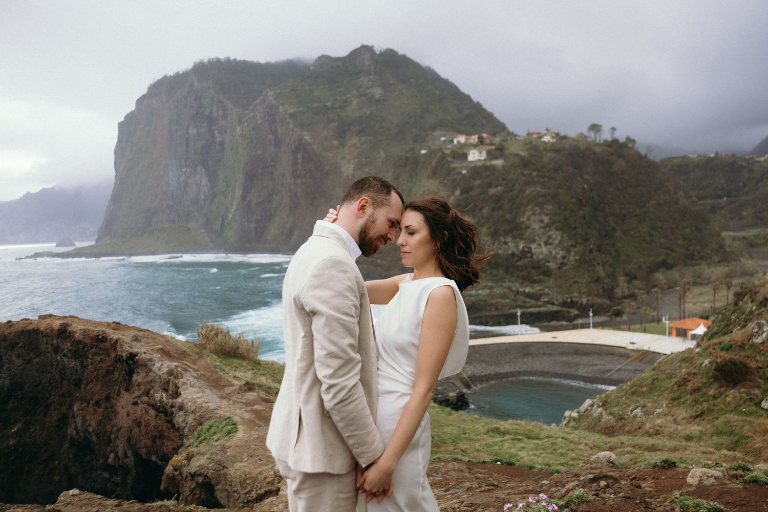 Bride and groom holding hands on a cliff overlooking a dramatic coastal landscape with mountains in Madeira.