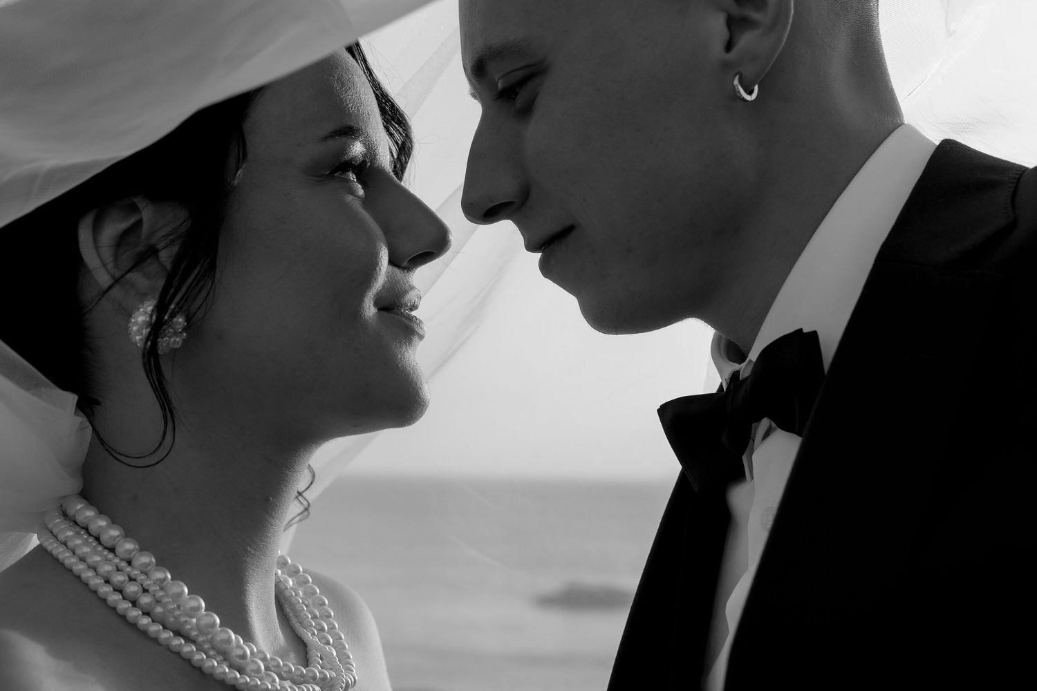 Black and white intimate close-up of bride with pearl necklace and groom nearly kissing.