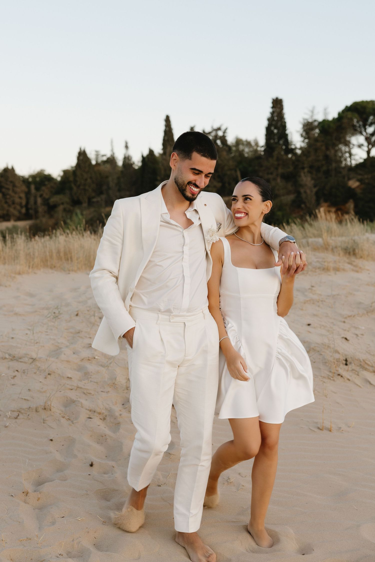 Romantic candid moment on the beach of Ferragudo with groom putting his arm around the bride as they walk