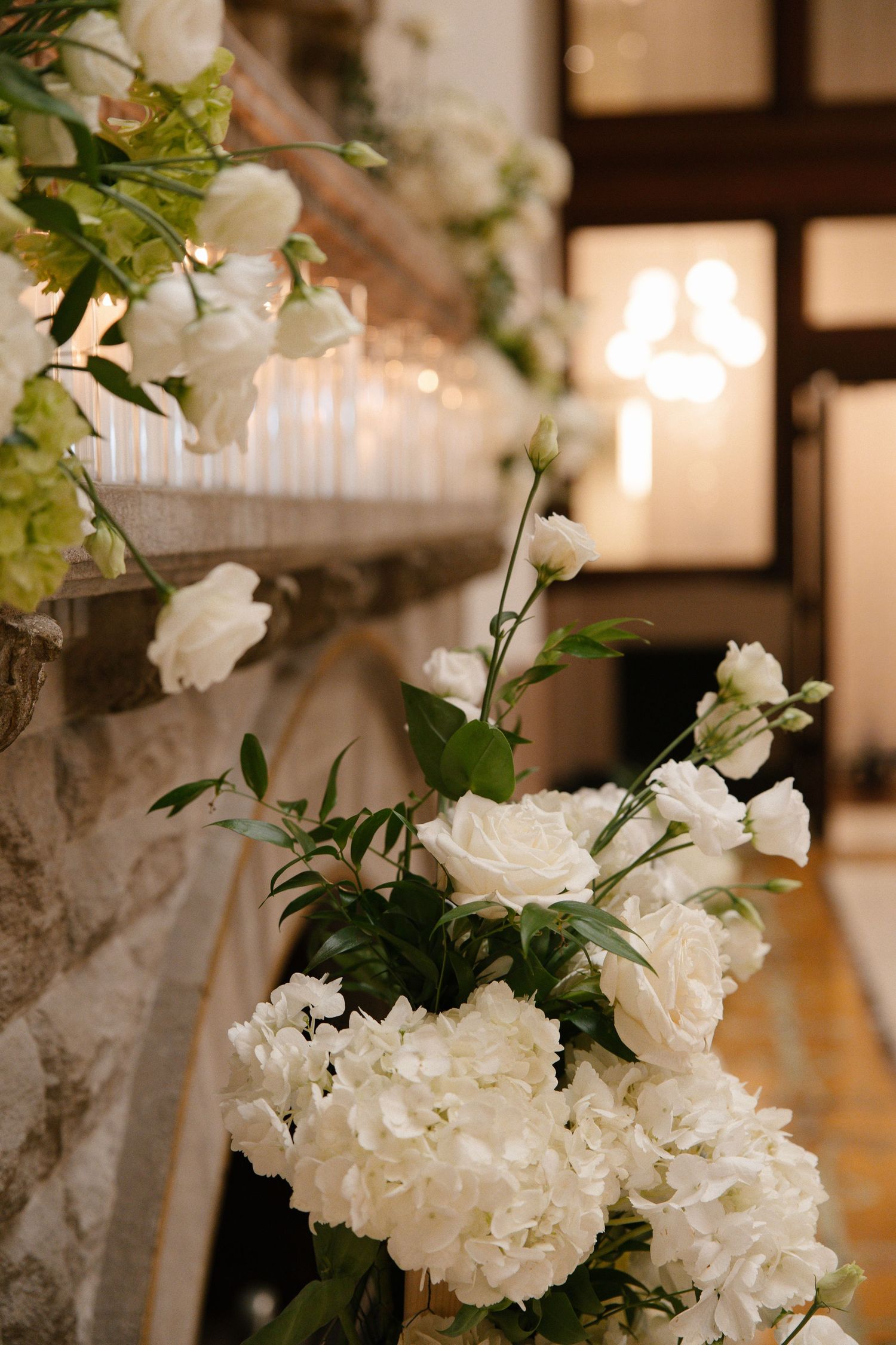 Elegant white floral arrangement featuring peonies and roses with green foliage displayed on stone steps at a wedding venue.