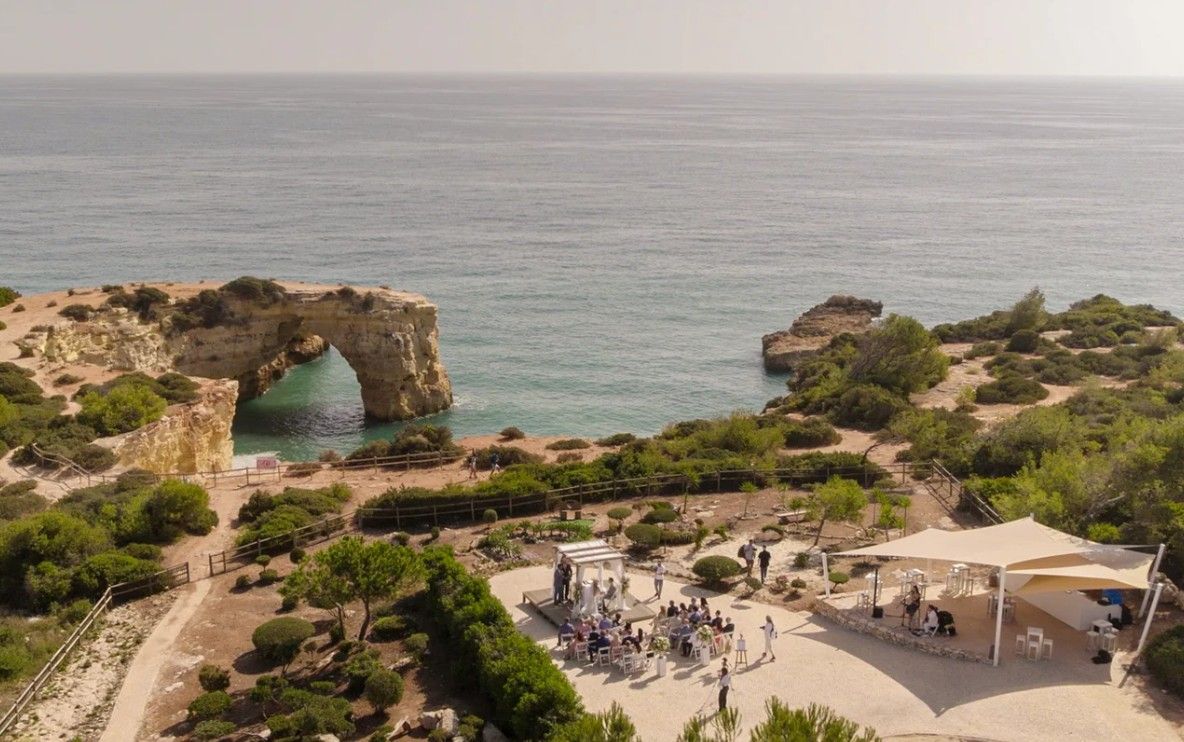 Aerial view of a wedding reception near a stunning natural rock arch on the Algarve coast.
