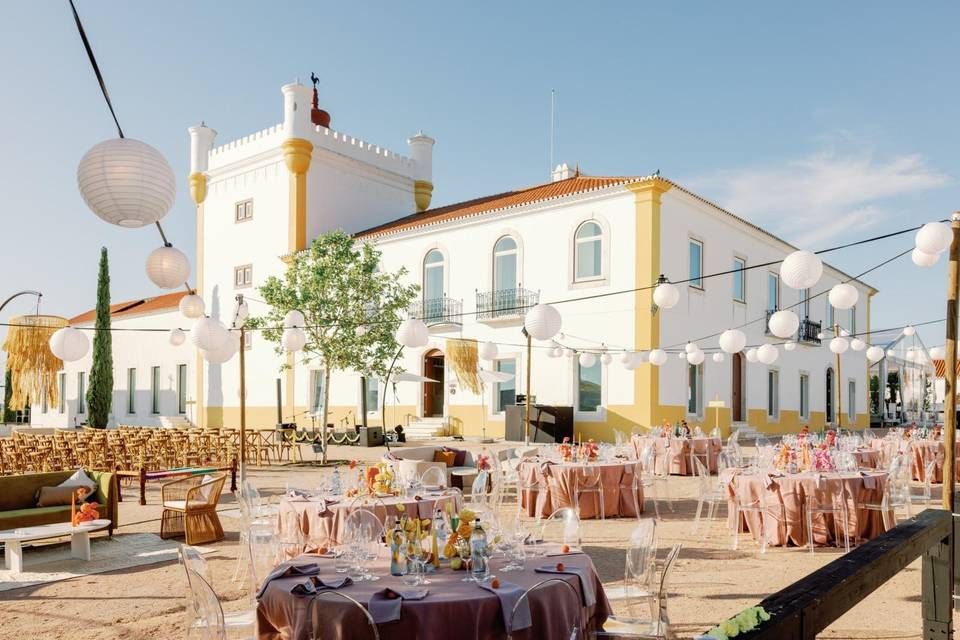 Outdoor wedding reception at a yellow Portuguese manor with paper lantern string lights and floral tables.