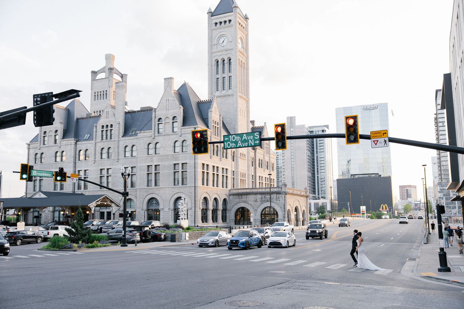 Historic stone building at Nashville city intersection with modern skyline, traffic lights, and pedestrian crossing on a cloudy day.