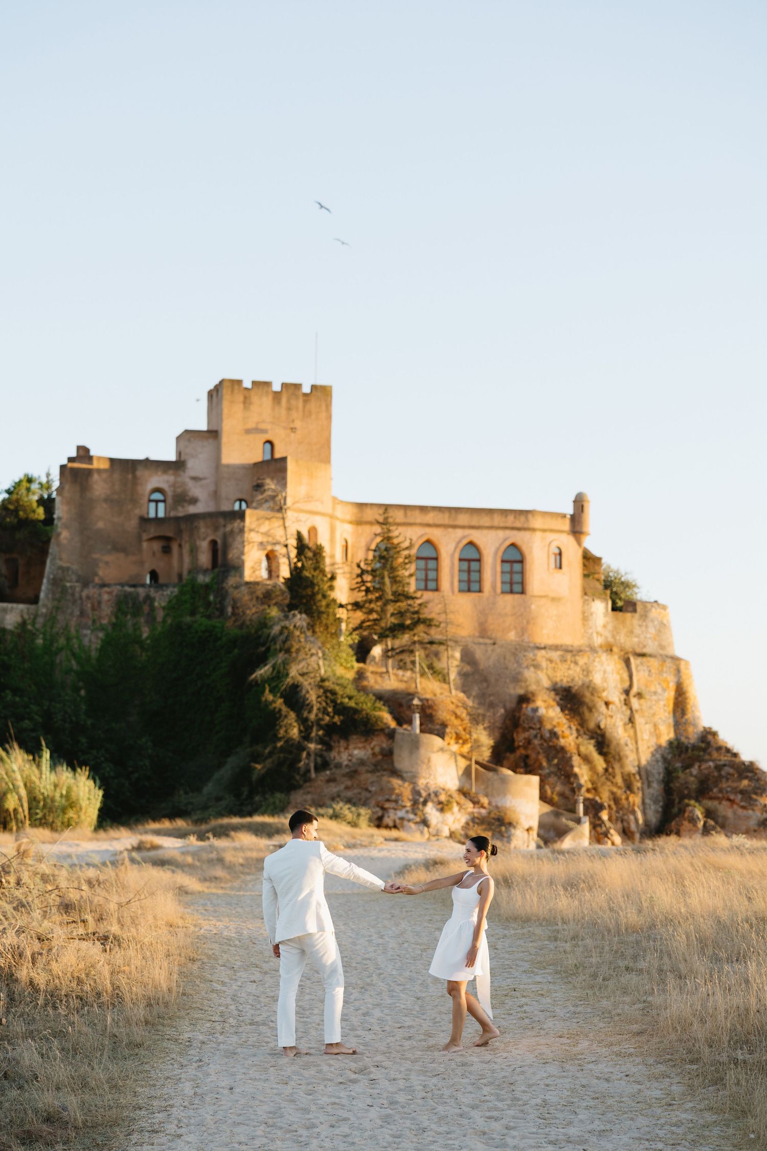 Bridal couple dancing in the sand of the praia da angrinha with the ferragudo castle in the background