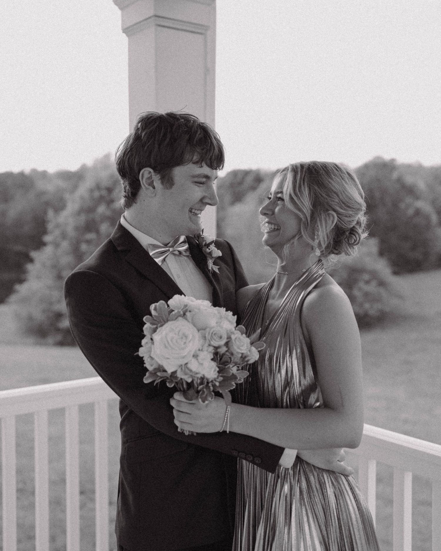 A romantic black and white photograph of a couple in formal attire sharing an intimate moment on a porch.