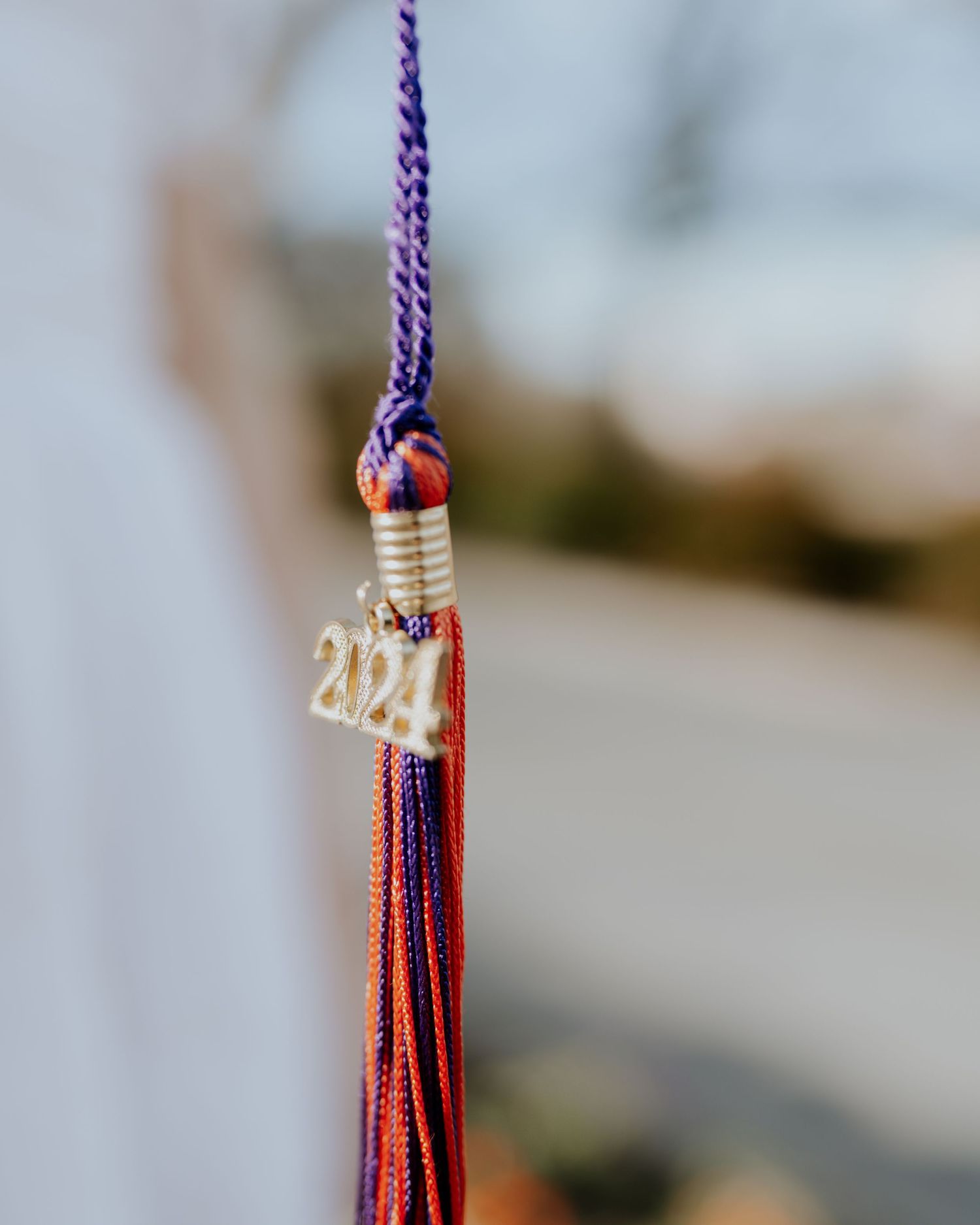 A red and purple graduation tassel with 2021 year charm hanging against a blurred background.
